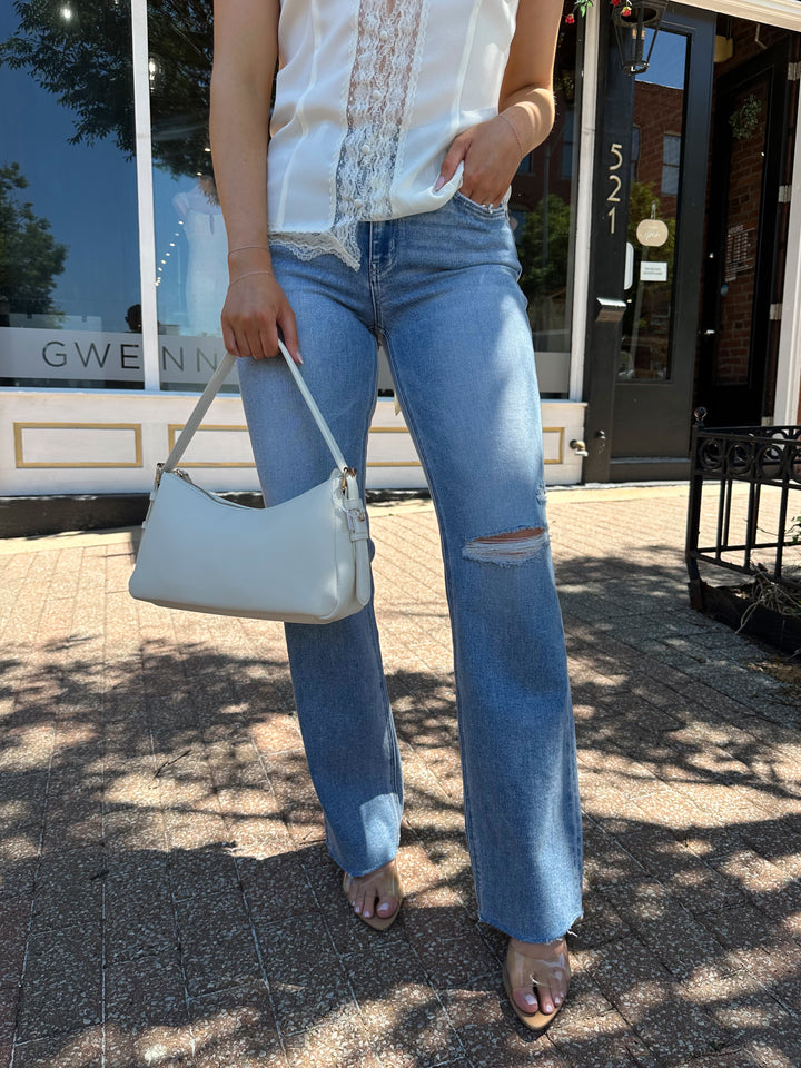 Woman wearing medium wash high rise jean with a slim wide leg fit, and slight distressing.