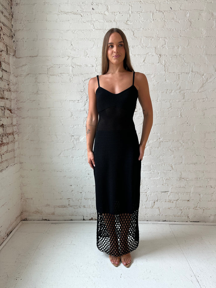 Woman wearing black knit maxi dress with netting bottom detail.