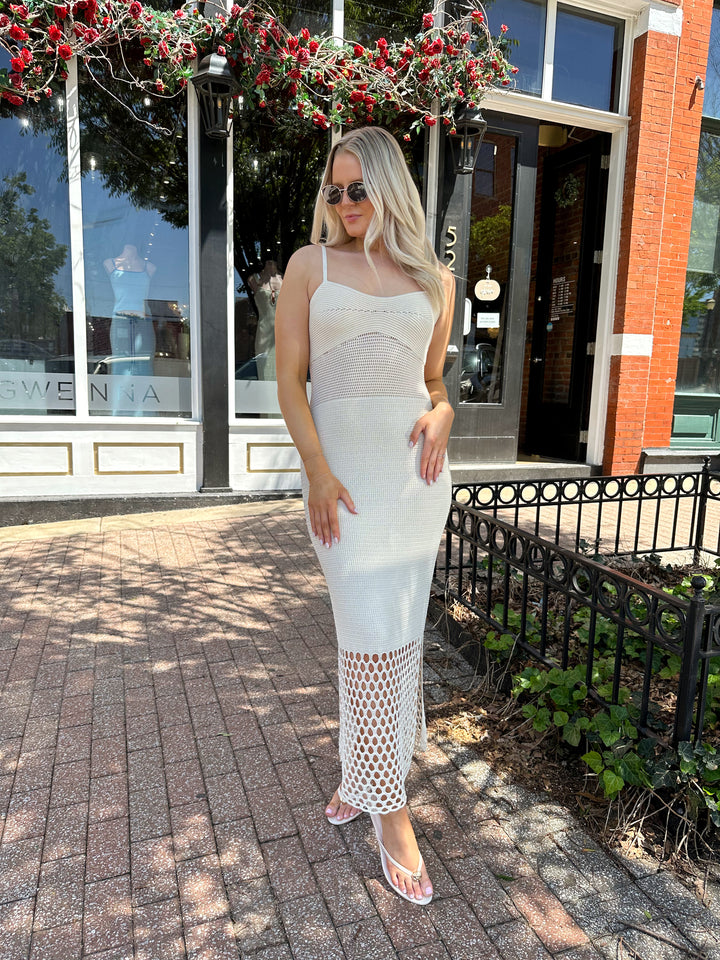 Woman wearing ecru colored knit midi dress with cutout netting bottom.