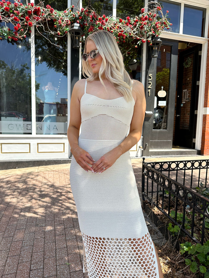 Woman wearing ecru colored knit midi dress with cutout netting bottom.