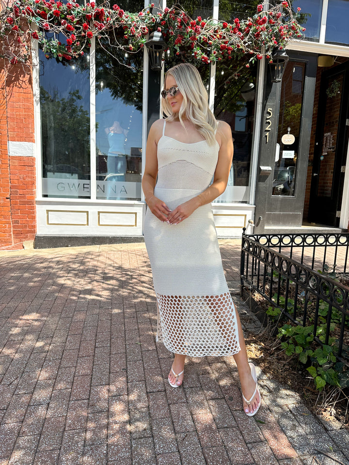 Woman wearing ecru colored knit midi dress with cutout netting bottom.