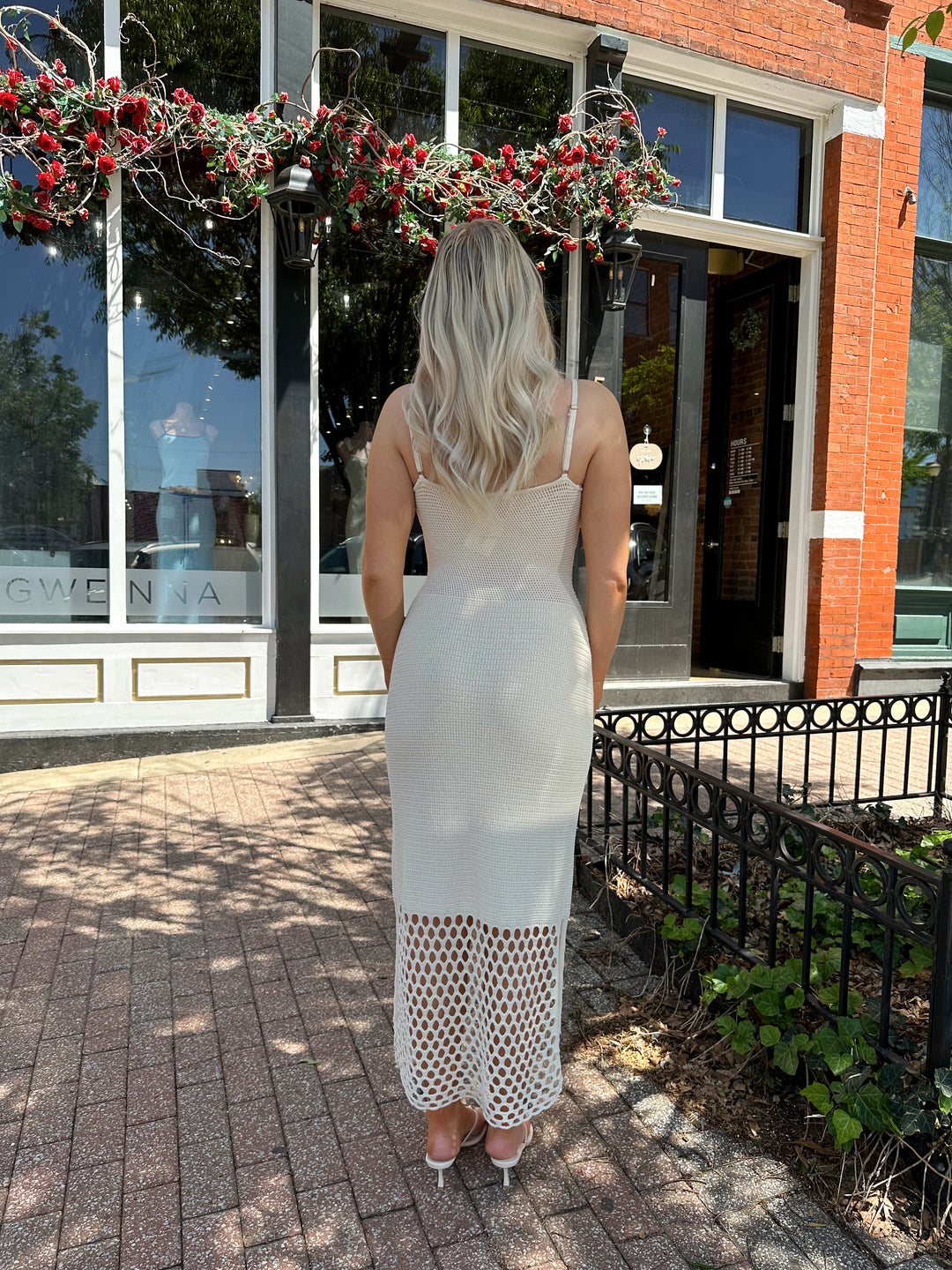 Woman wearing ecru colored knit midi dress with cutout netting bottom.