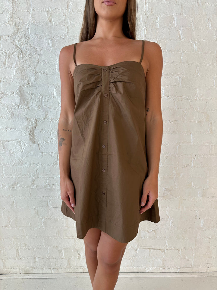 Woman wearing brown shift style mini dress with gathered detailing along the front. 