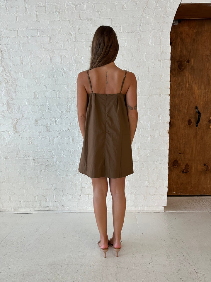 Woman wearing brown shift style mini dress with gathered detailing along the front. 