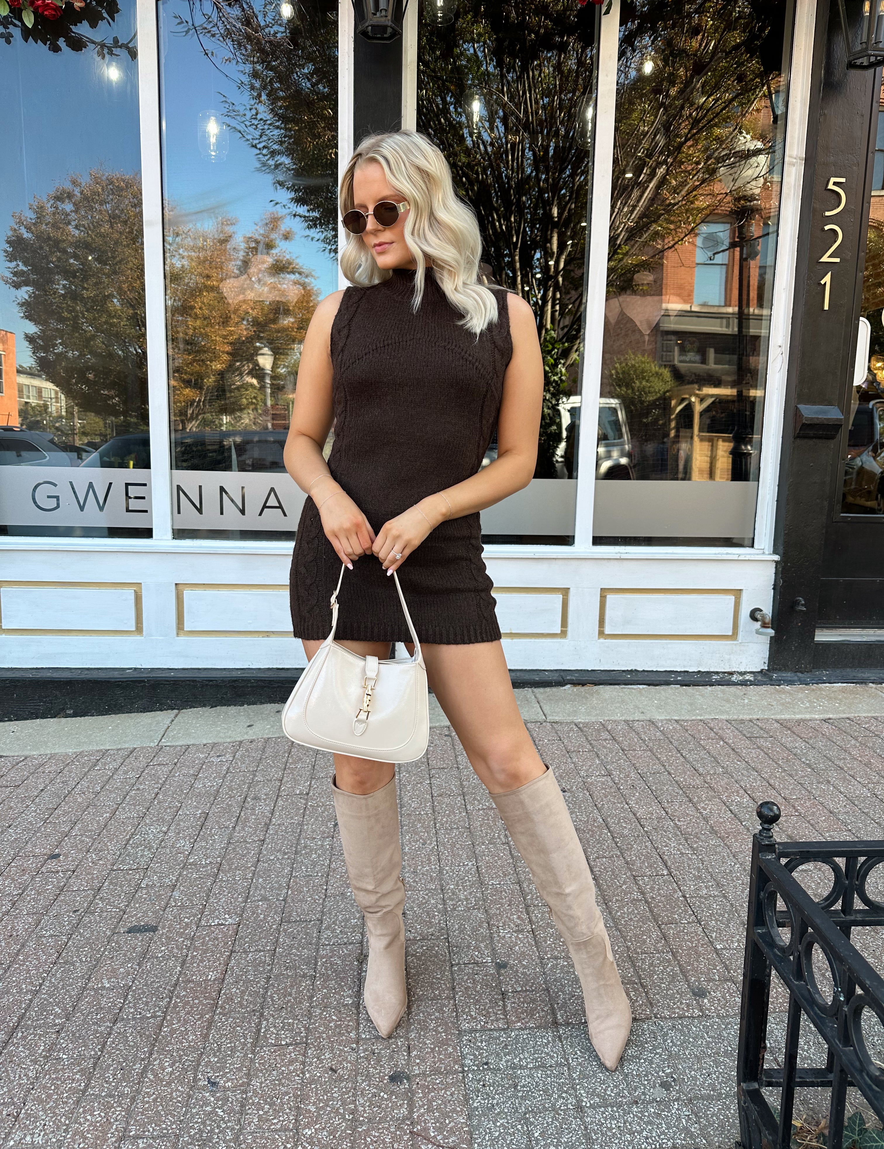 Woman wearing dark brown sleeveless sweater dress with suede knee boot.