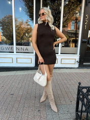 Woman wearing dark brown sleeveless sweater dress with suede knee boot.