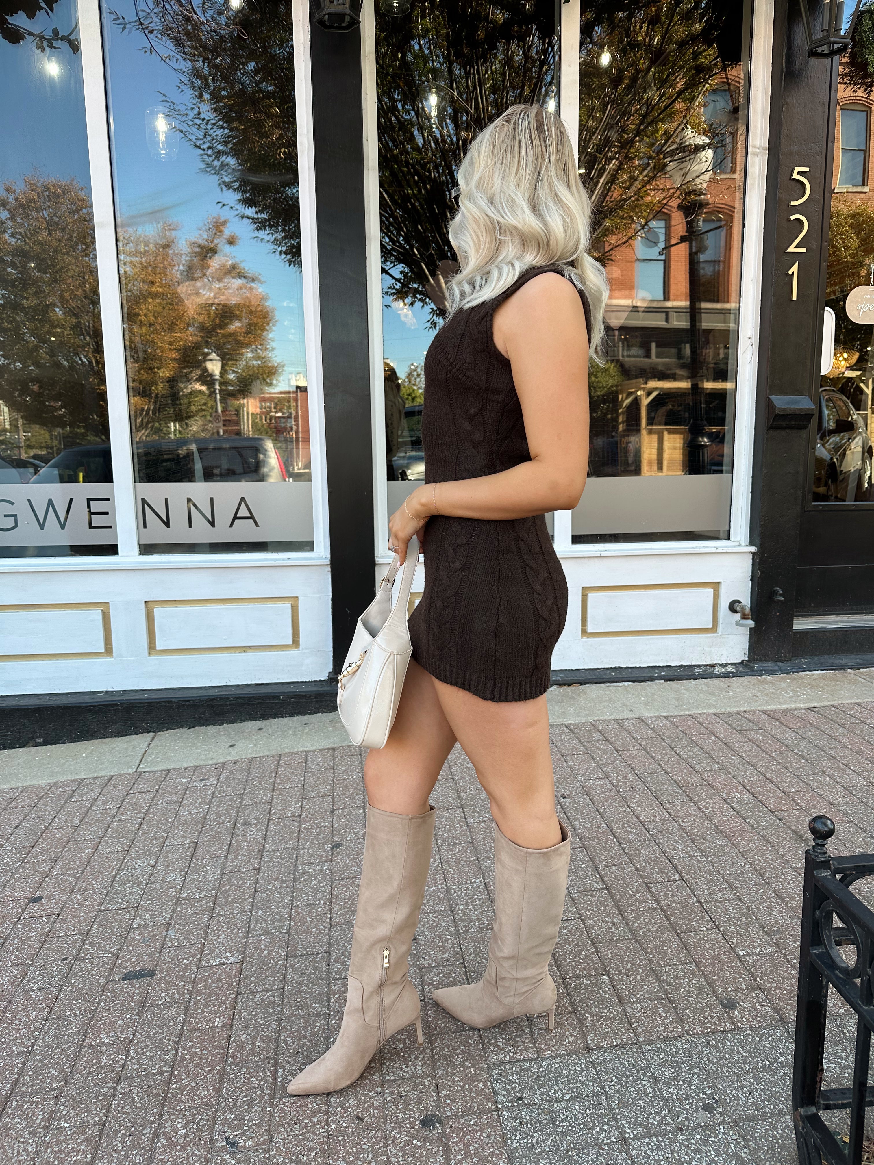Woman wearing dark brown sleeveless sweater dress with suede knee boot.