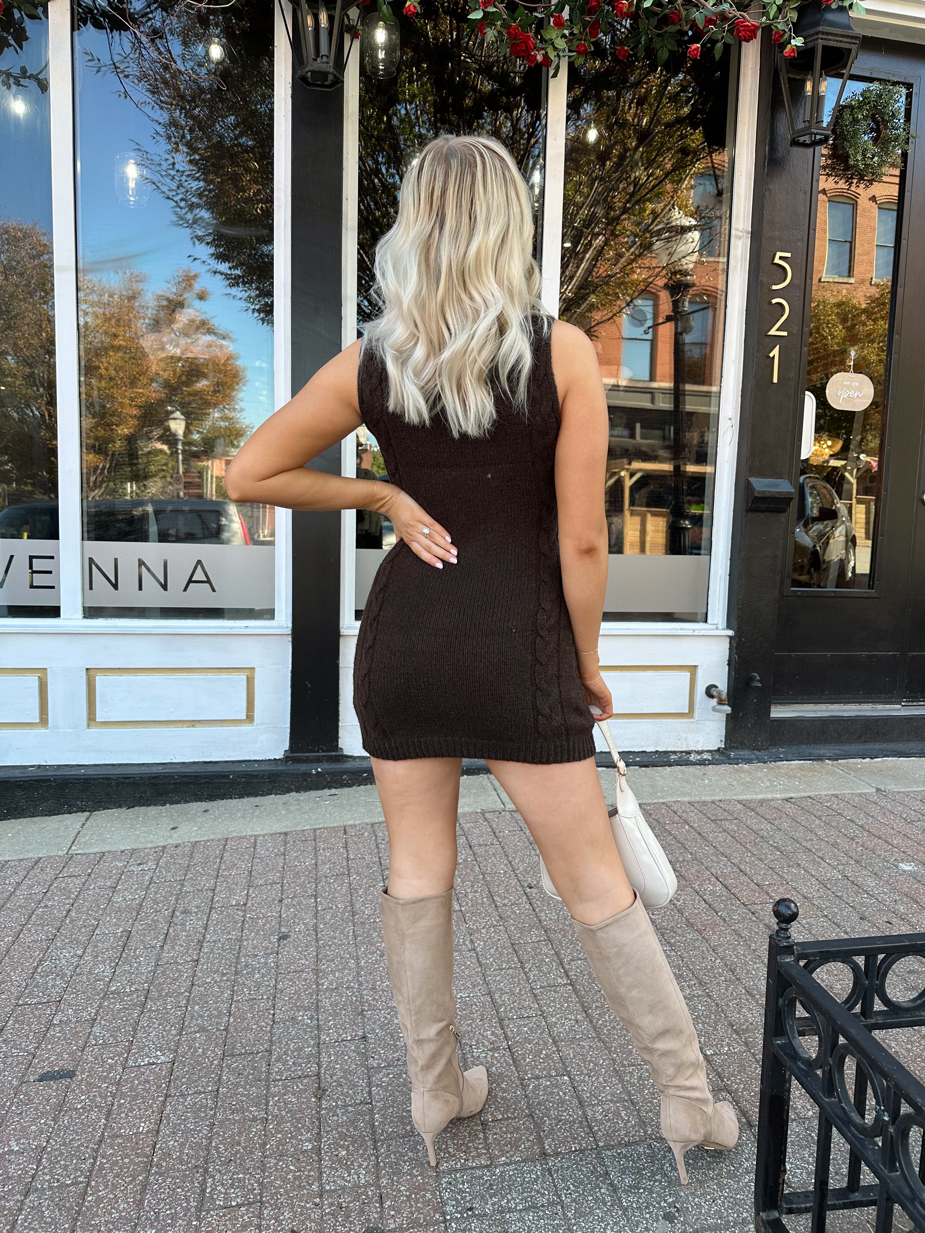 Woman wearing dark brown sleeveless sweater dress with suede knee boot.