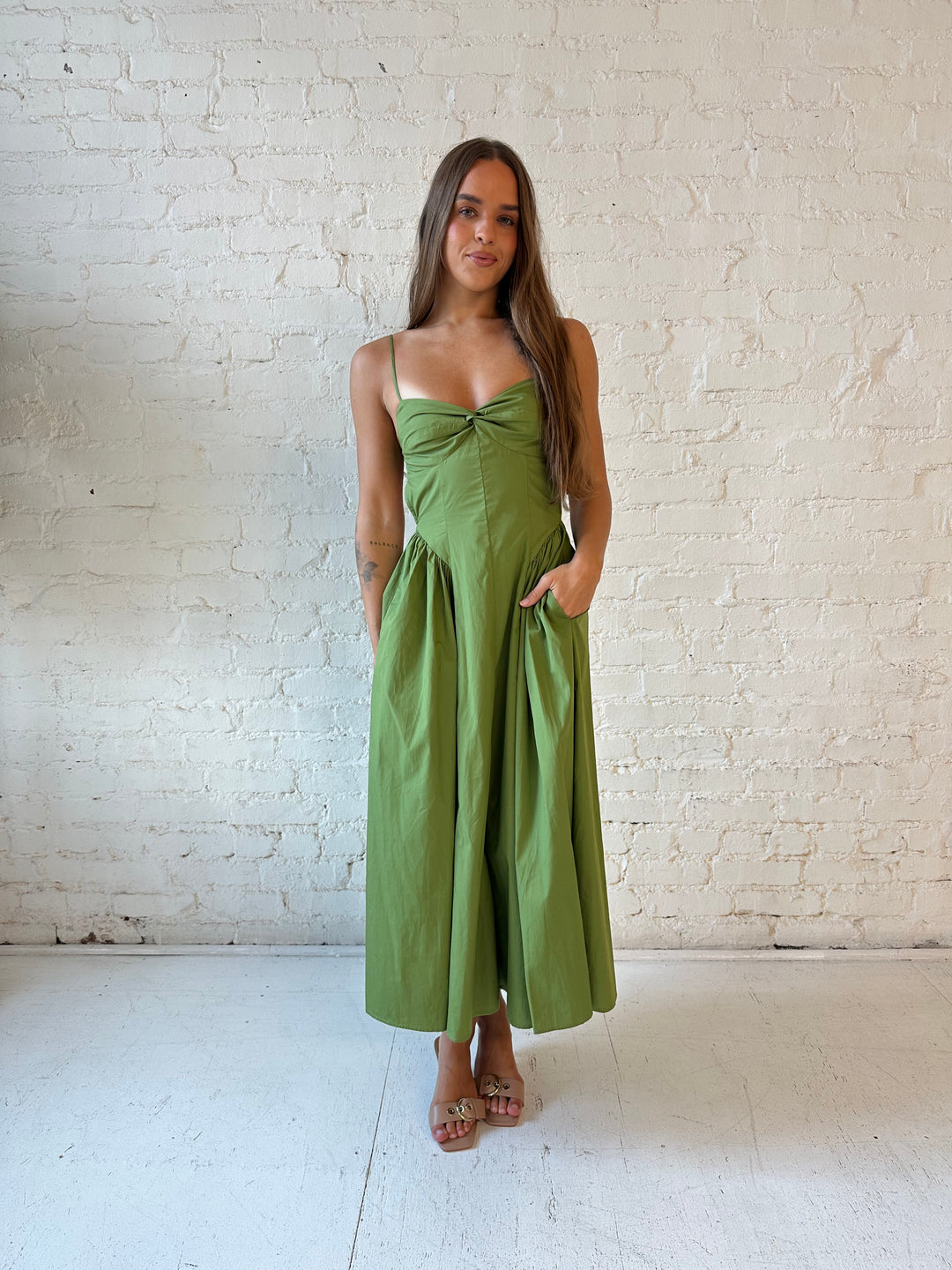 Woman wearing olive green drop waist midi dress with an open back. 