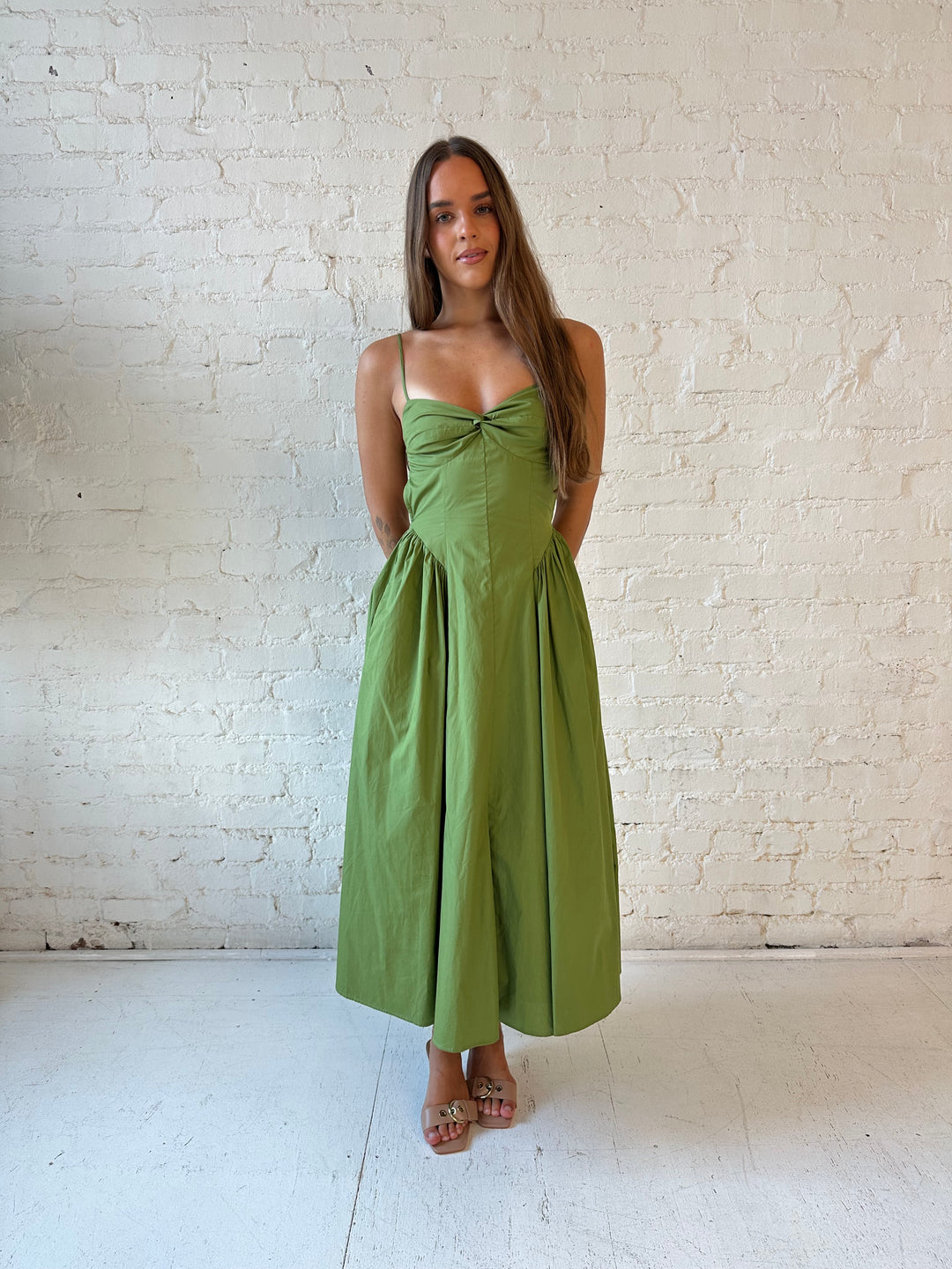 Woman wearing olive green drop waist midi dress with an open back. 