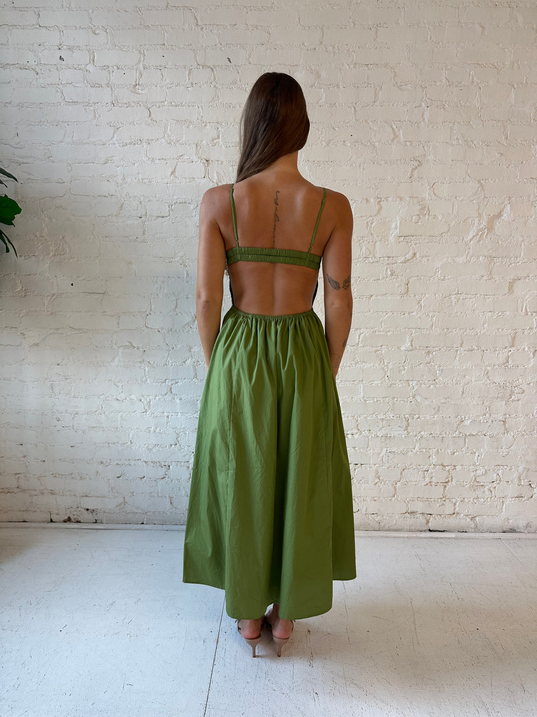 Woman wearing olive green drop waist midi dress with an open back. 