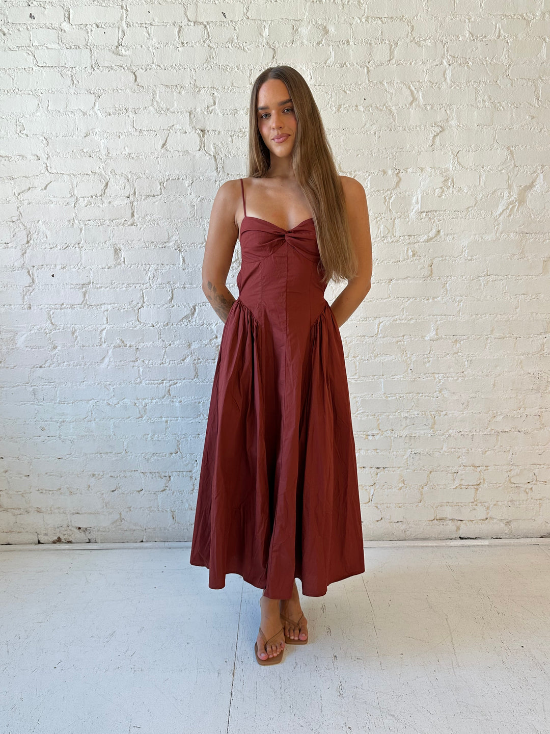 Woman wearing rust colored drop waist midi dress with sweetheart neckline, and open back.
