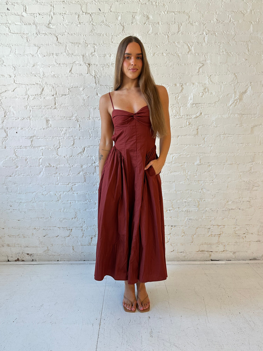 Woman wearing rust colored drop waist midi dress with sweetheart neckline, and open back.
