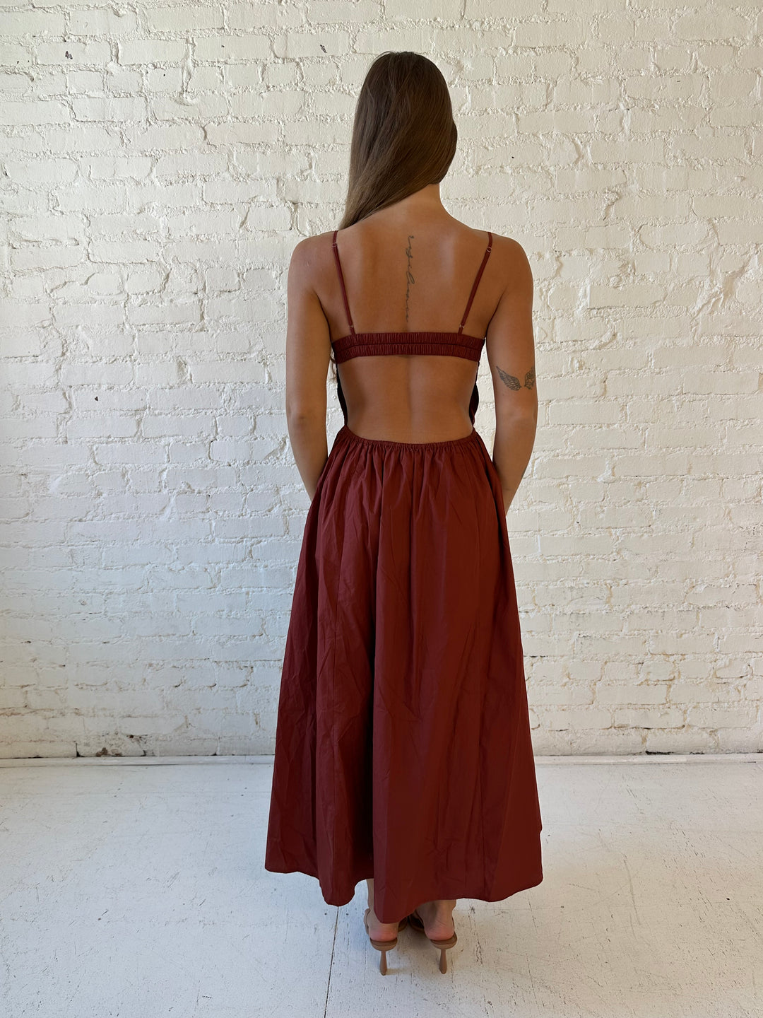 Woman wearing rust colored drop waist midi dress with sweetheart neckline, and open back.