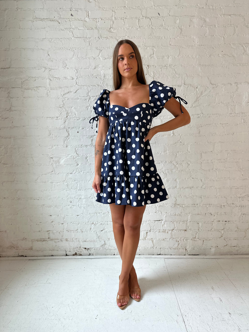 Woman wearing navy blue polka dot babydoll mini dress with sweetheart neckline, and puff sleeves.
