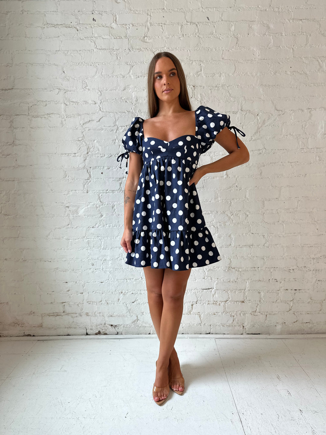 Woman wearing navy blue polka dot babydoll mini dress with sweetheart neckline, and puff sleeves.