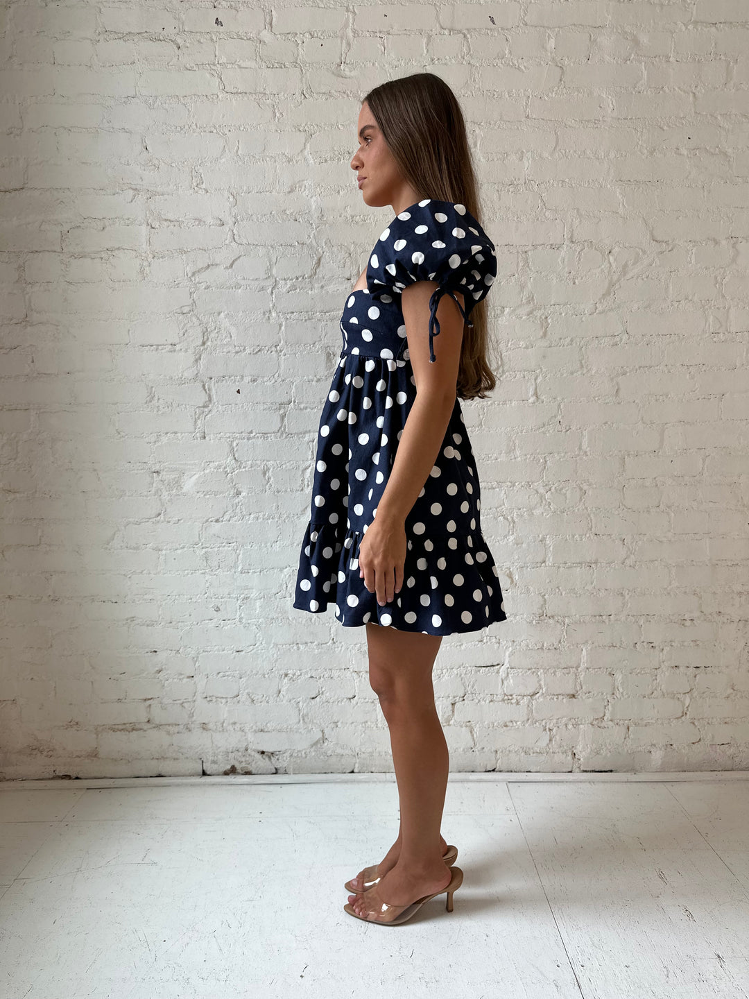 Woman wearing navy blue polka dot babydoll mini dress with sweetheart neckline, and puff sleeves.