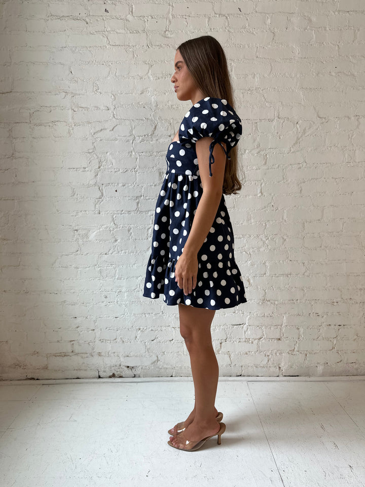 Woman wearing navy blue polka dot babydoll mini dress with sweetheart neckline, and puff sleeves.