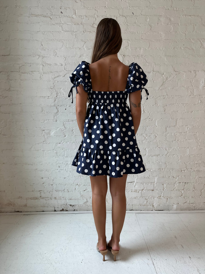 Woman wearing navy blue polka dot babydoll mini dress with sweetheart neckline, and puff sleeves.
