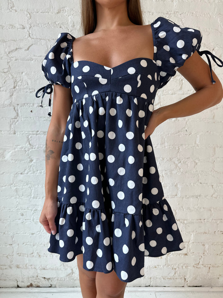 Woman wearing navy blue polka dot babydoll mini dress with sweetheart neckline, and puff sleeves.
