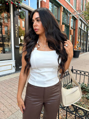 Woman wearing white halter neck top with chain link detail, and brown leather pants. 
