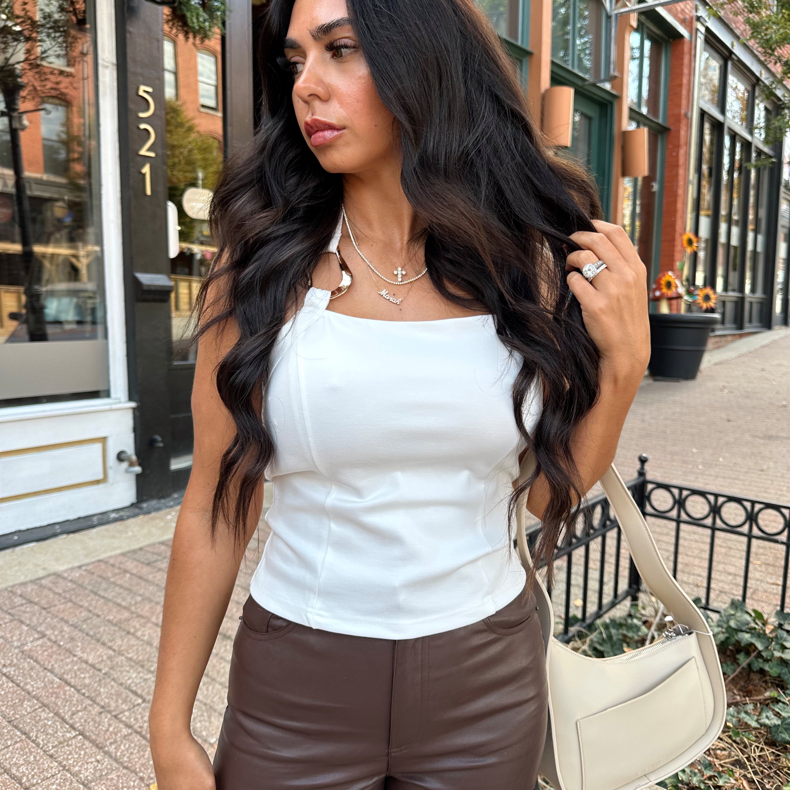 Woman wearing white halter neck top with chain link detail, and brown leather pants. 