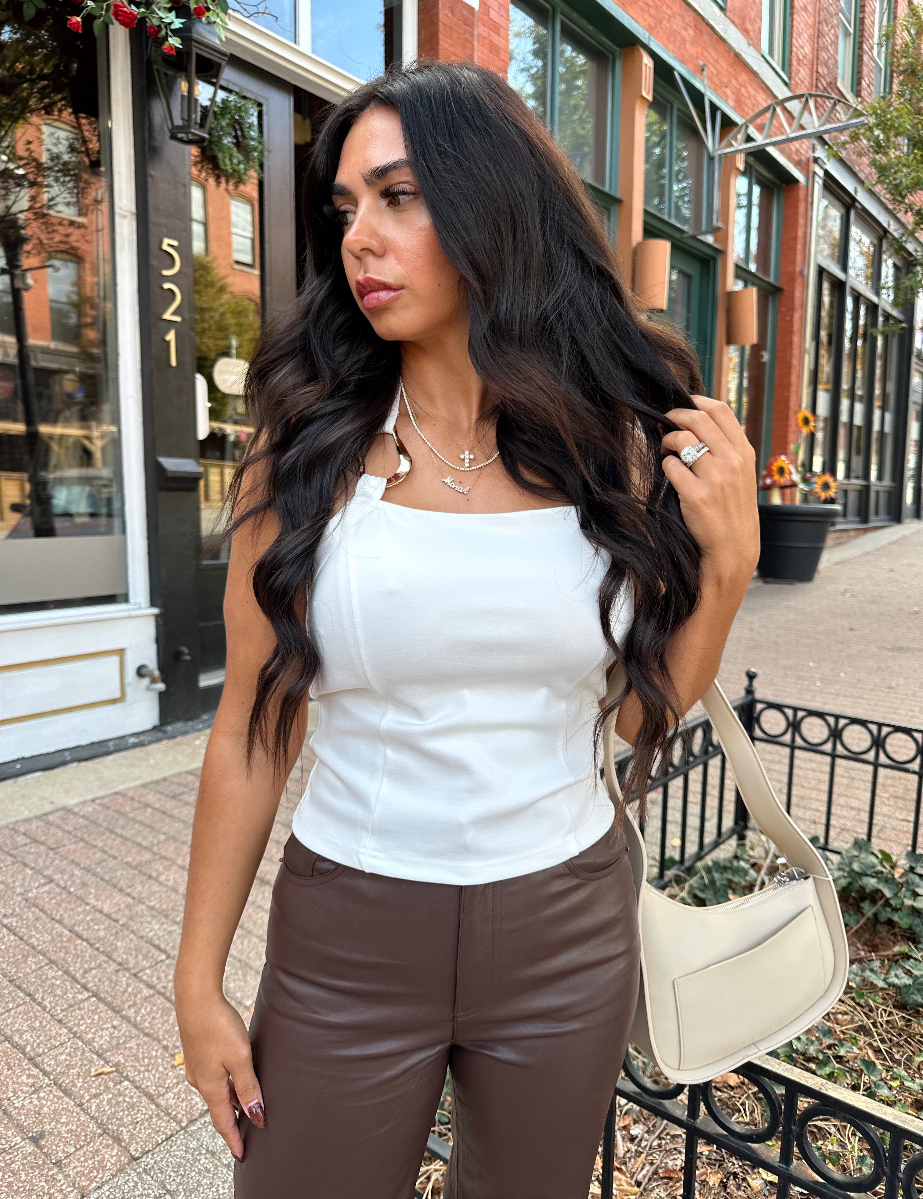 Woman wearing white halter neck top with chain link detail, and brown leather pants. 