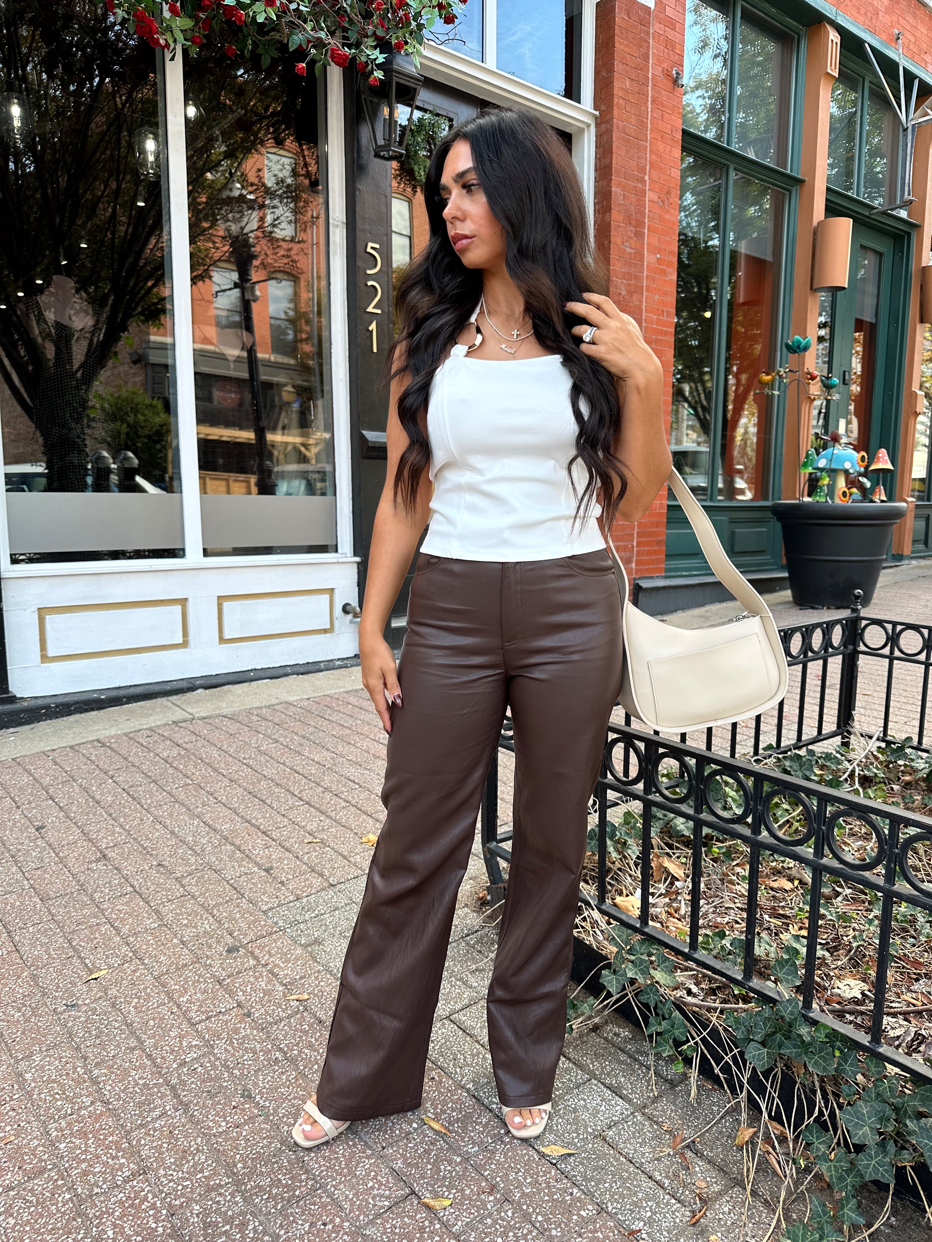 Woman wearing white halter neck top with chain link detail, and brown leather pants. 