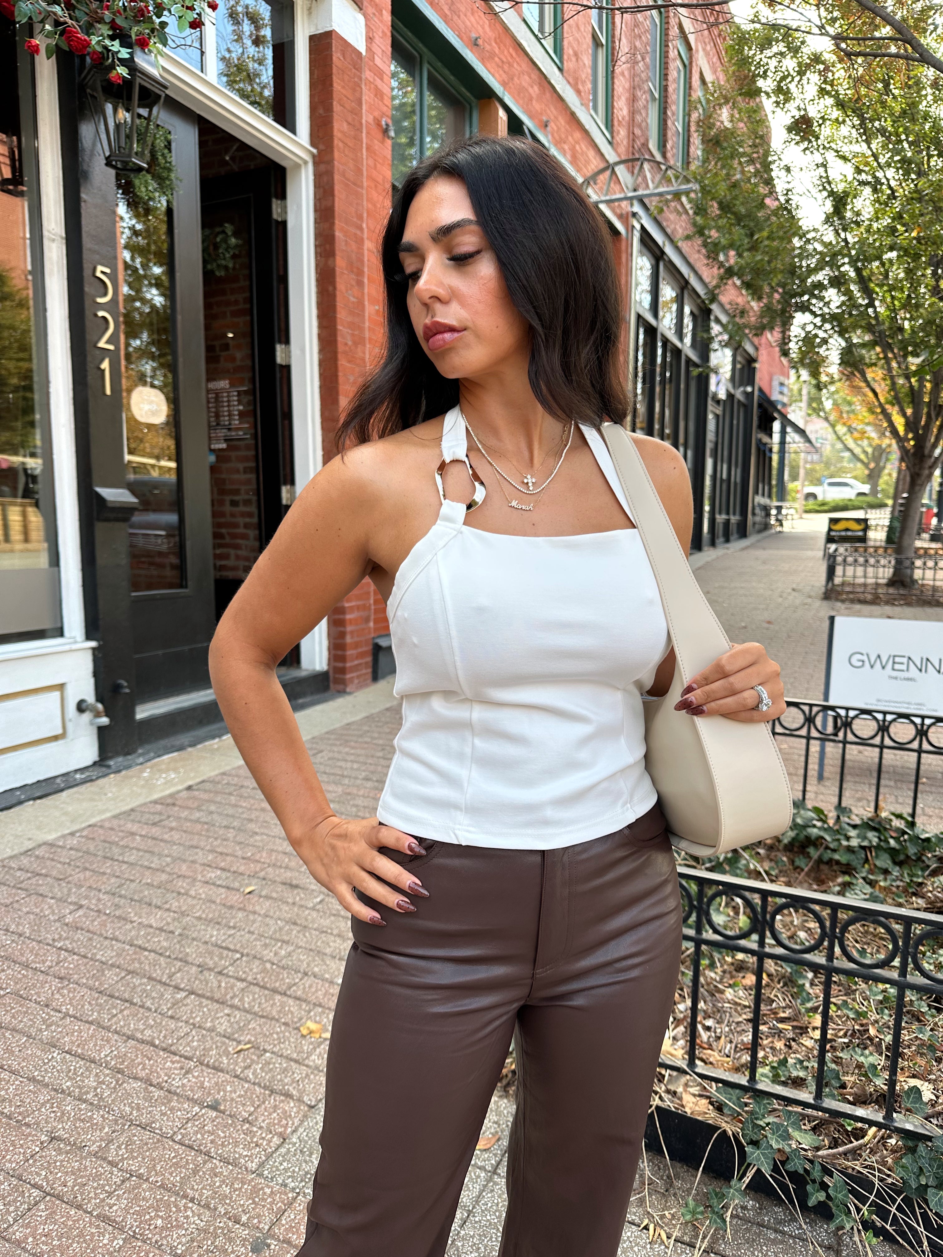 Woman wearing white halter neck top with chain link detail, and brown leather pants. 
