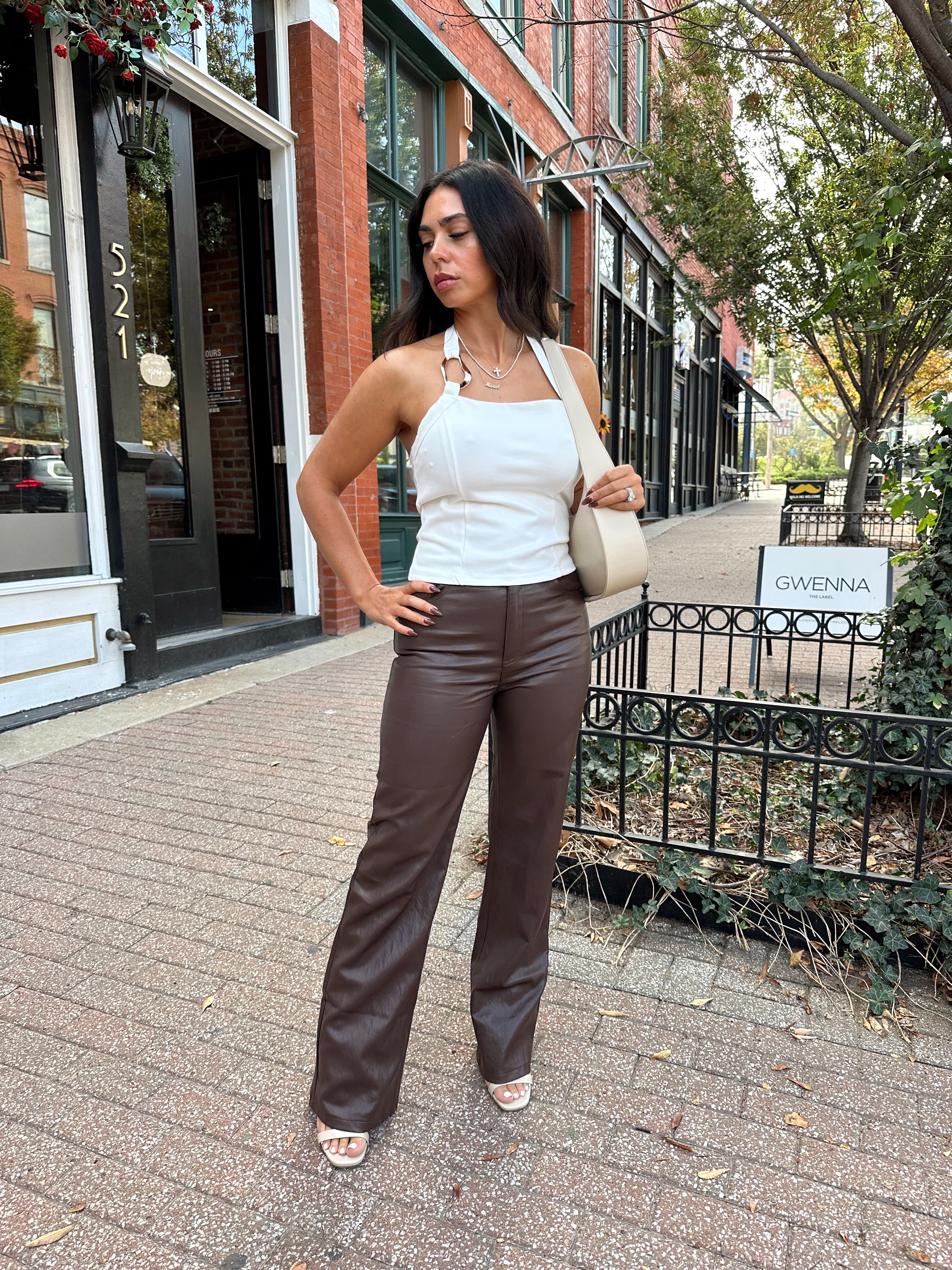 Woman wearing white halter neck top with chain link detail, and brown leather pants. 