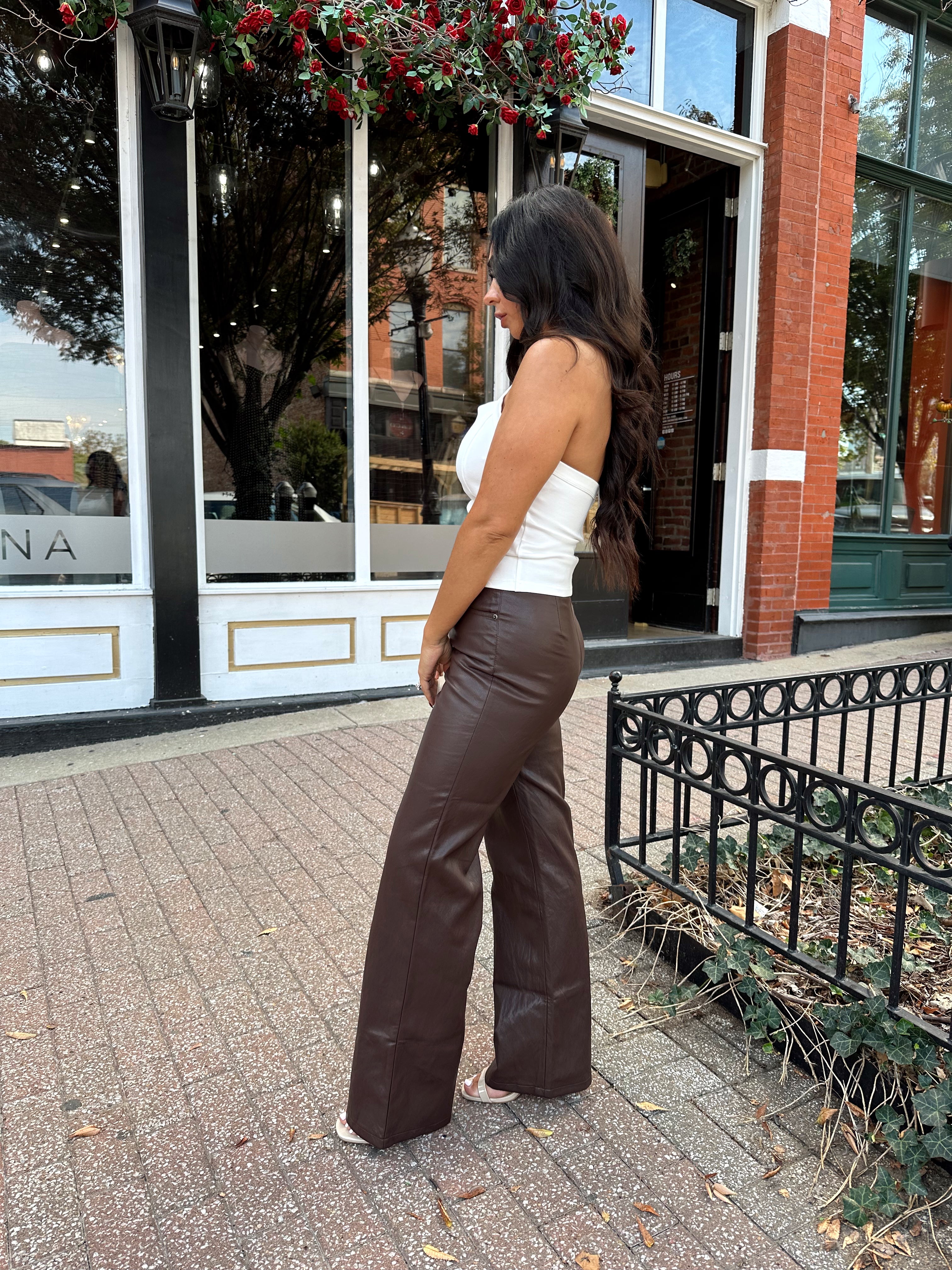 Woman wearing white halter neck top with chain link detail, and brown leather pants. 