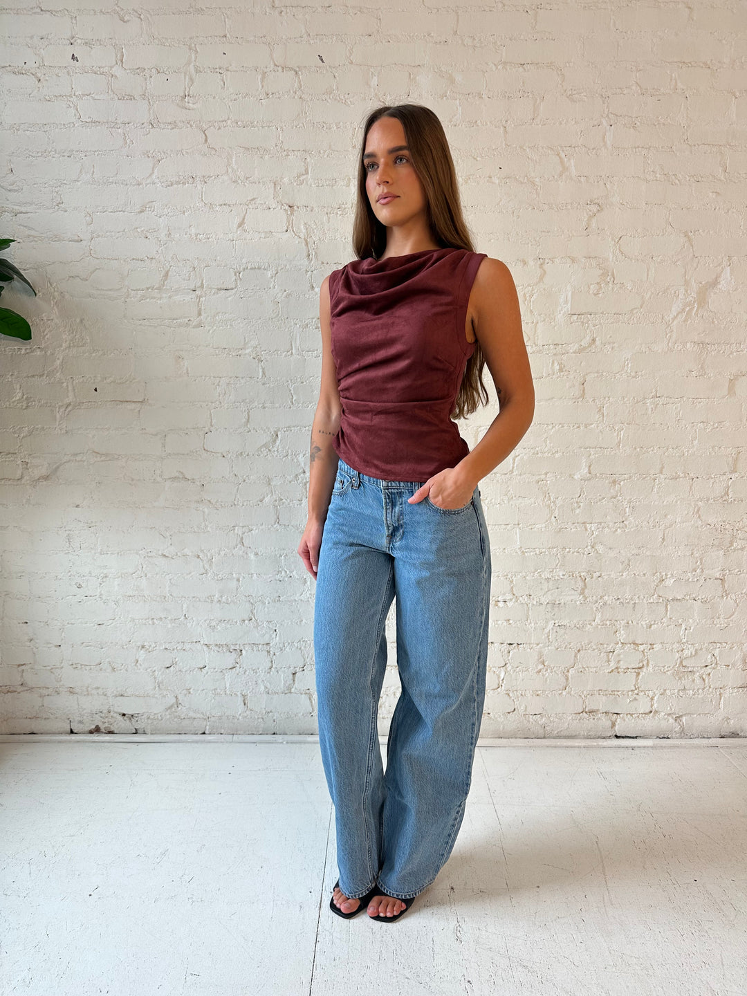 Woman wearing burgundy suede sleeveless top with cowl neckline, and asymmetrical hem.