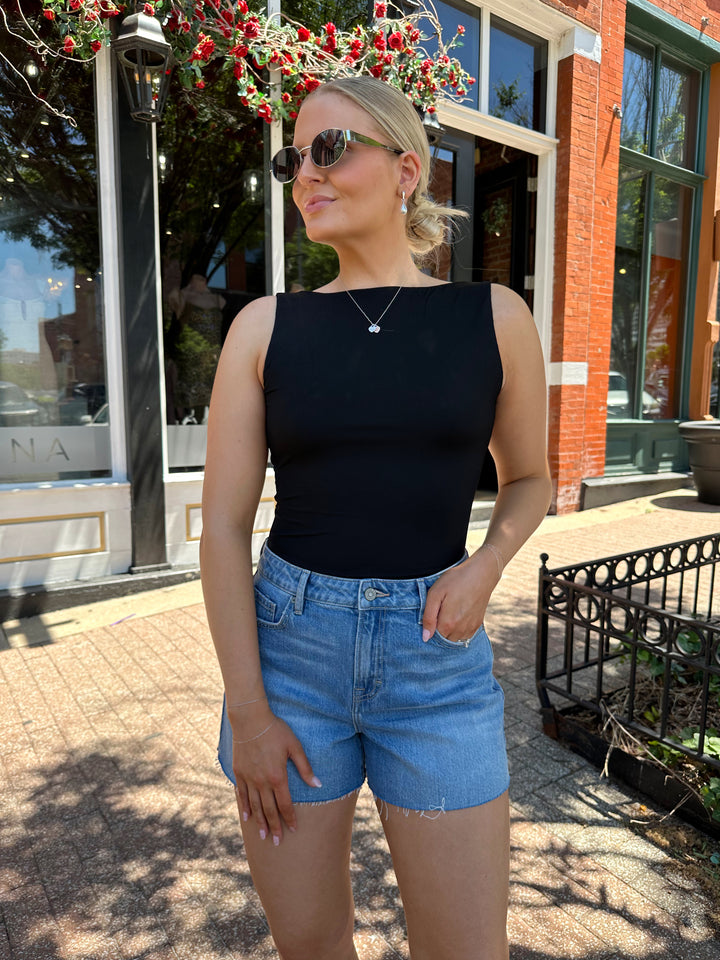 Woman wearing black boatneck bodysuit with open back and beaded strap detailing. 