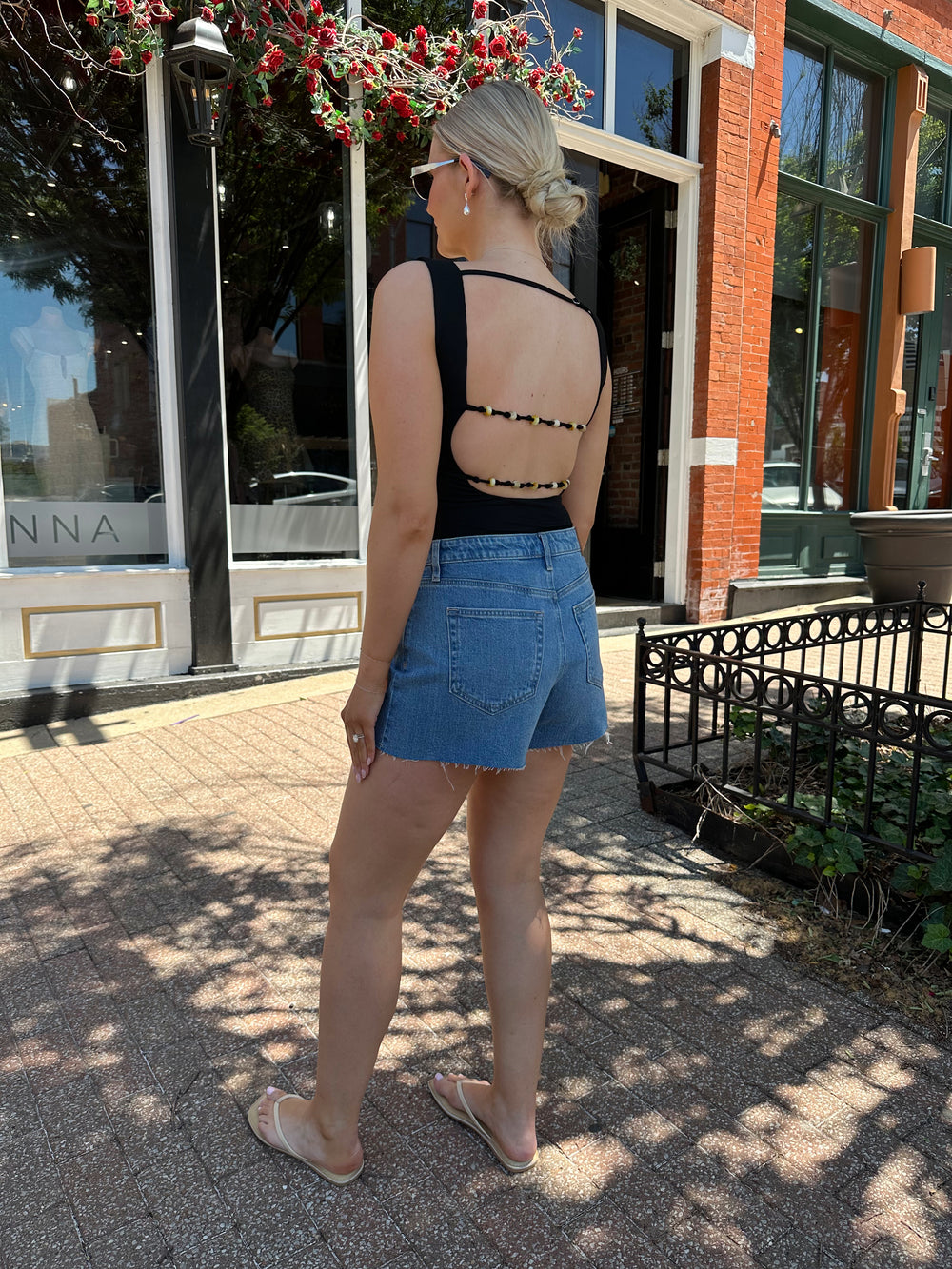 Woman wearing black boatneck bodysuit with open back and beaded strap detailing. 