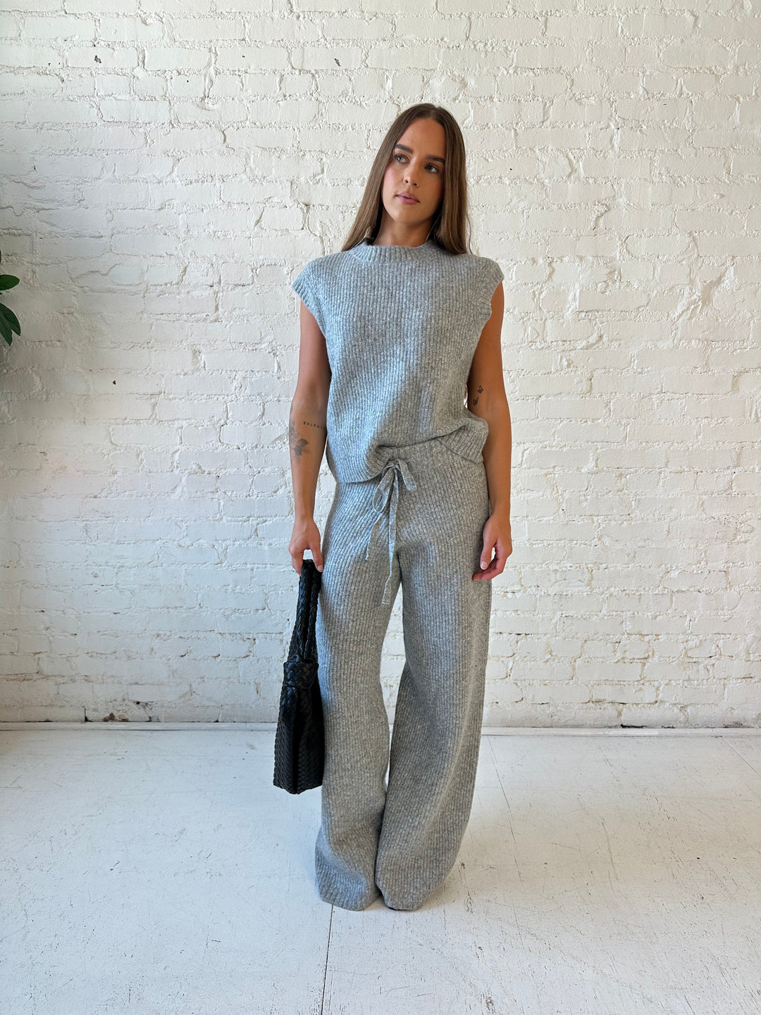 Woman wearing grey knit sweater two piece lounge set with short sleeve top, and wide leg pant. 