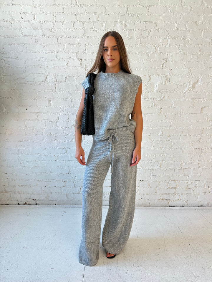 Woman wearing grey knit sweater two piece lounge set with short sleeve top, and wide leg pant. 