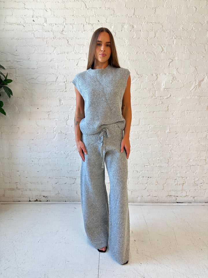 Woman wearing grey knit sweater two piece lounge set with short sleeve top, and wide leg pant. 