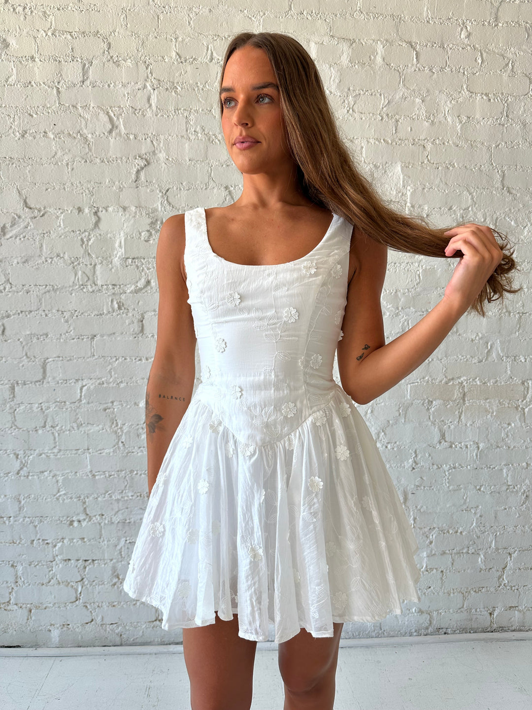 Woman wearing white fit to flare mini dress with embroidered floral detail. 