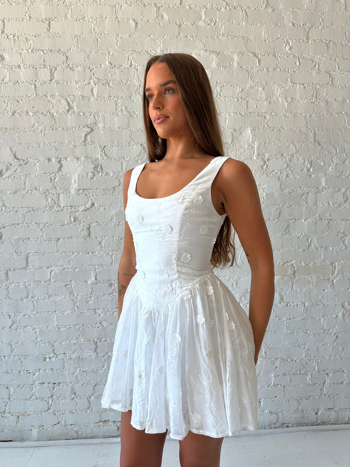 Woman wearing white fit to flare mini dress with embroidered floral detail. 