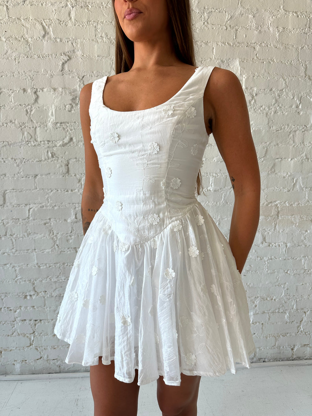 Woman wearing white fit to flare mini dress with embroidered floral detail. 