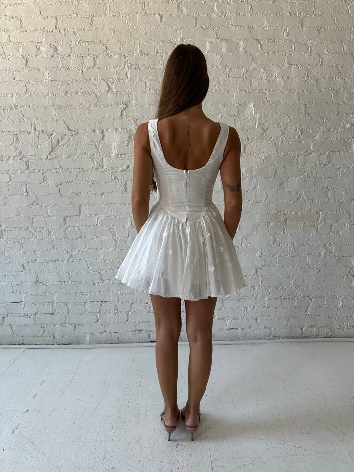 Woman wearing white fit to flare mini dress with embroidered floral detail. 
