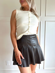 Woman wearing a dark brown vegan leather pleated mini skirt.