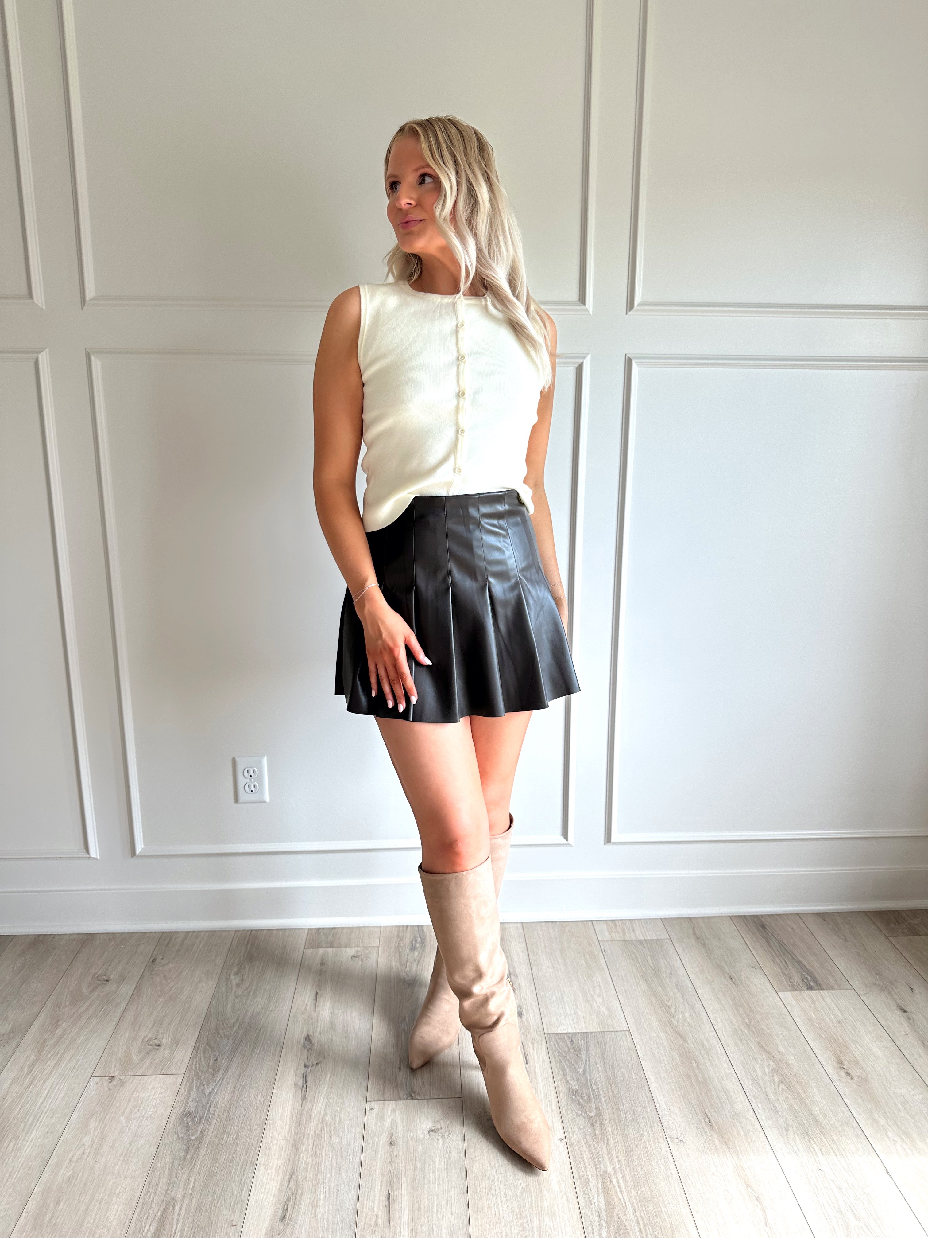 Woman wearing a dark brown vegan leather pleated mini skirt.