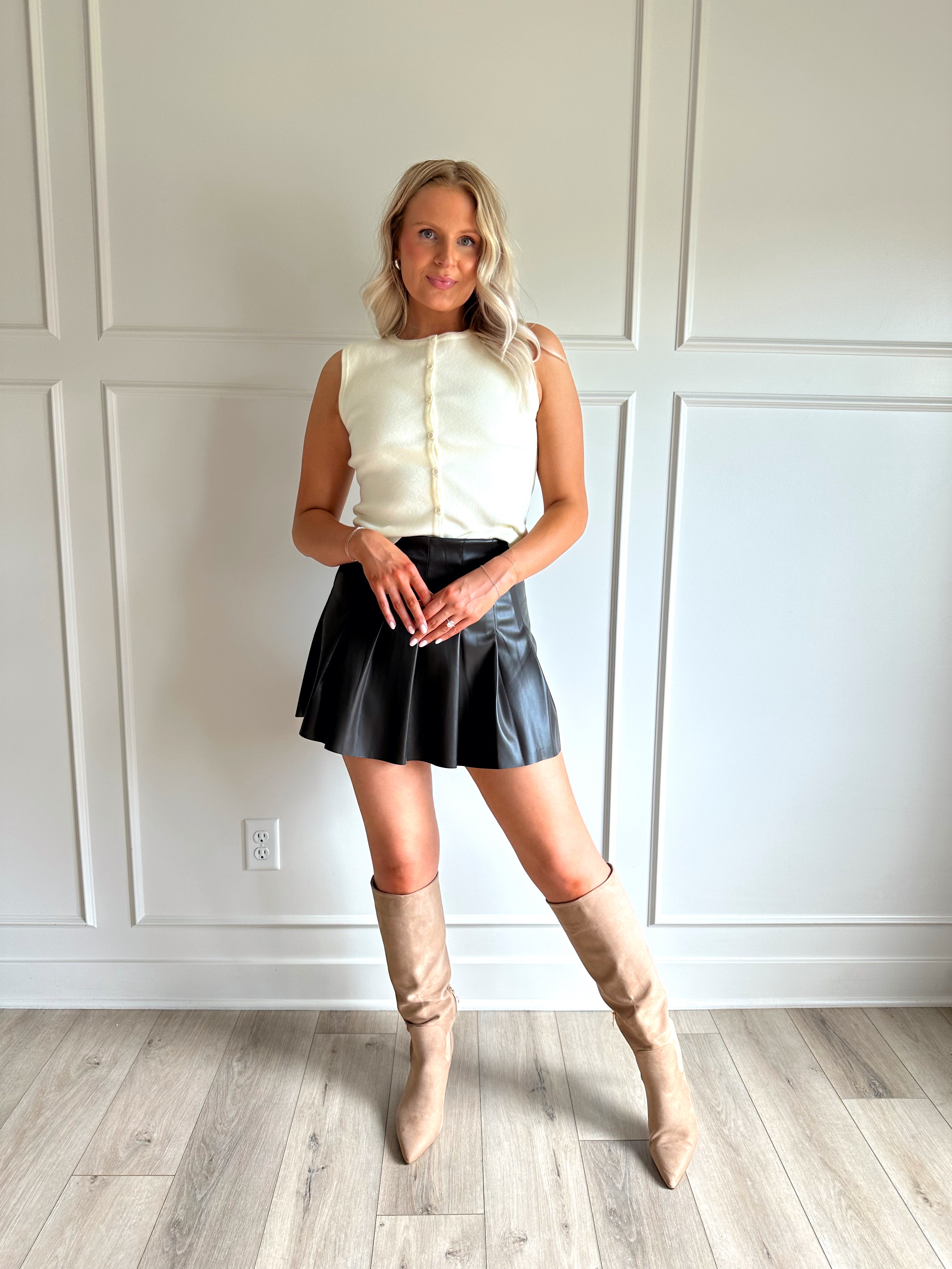 Woman wearing a dark brown vegan leather pleated mini skirt.