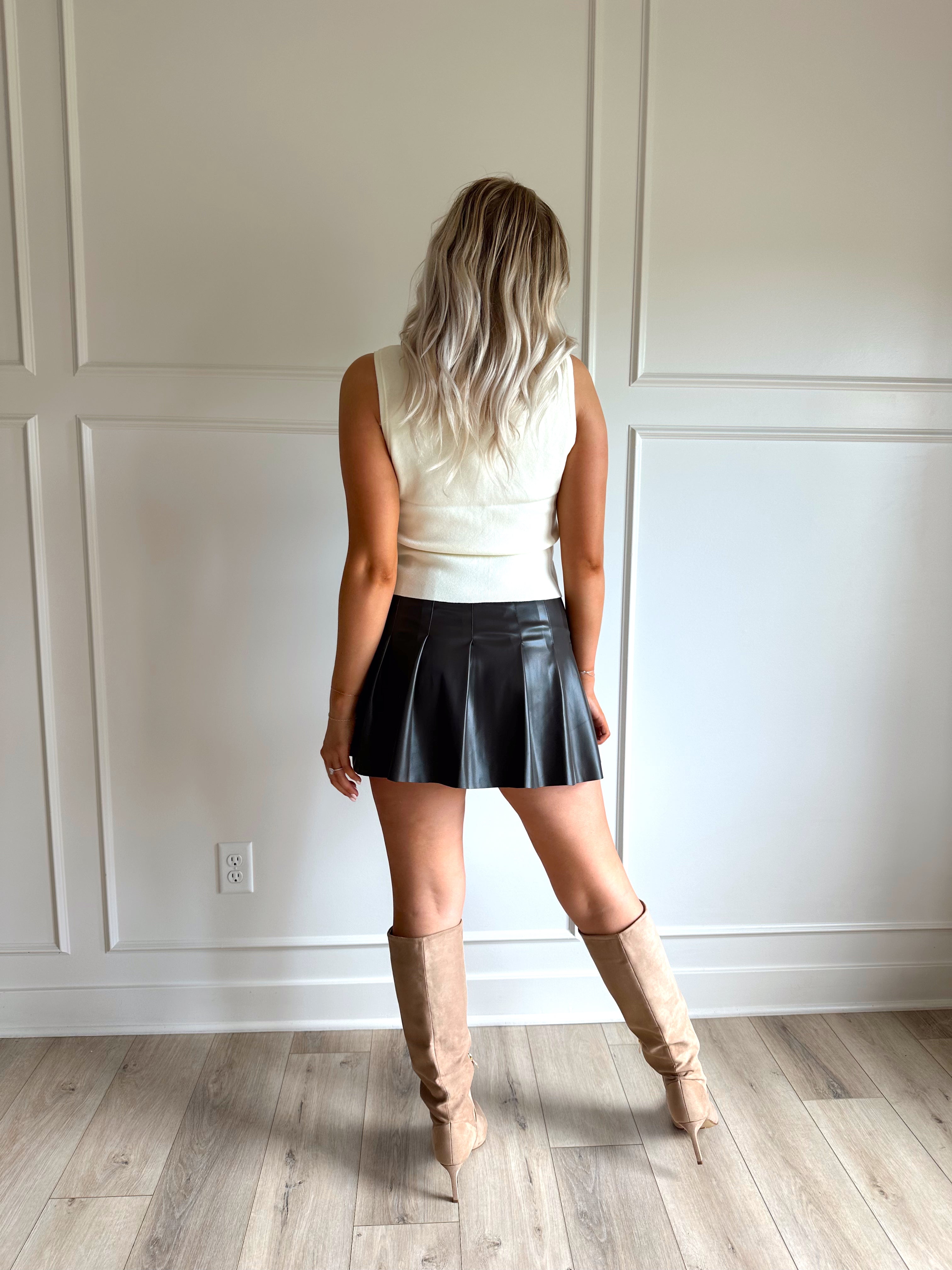Woman wearing a dark brown vegan leather pleated mini skirt.
