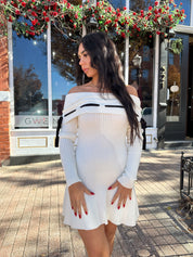 Woman wearing cream off the shoulder sweater mini dress with black tie detail. 