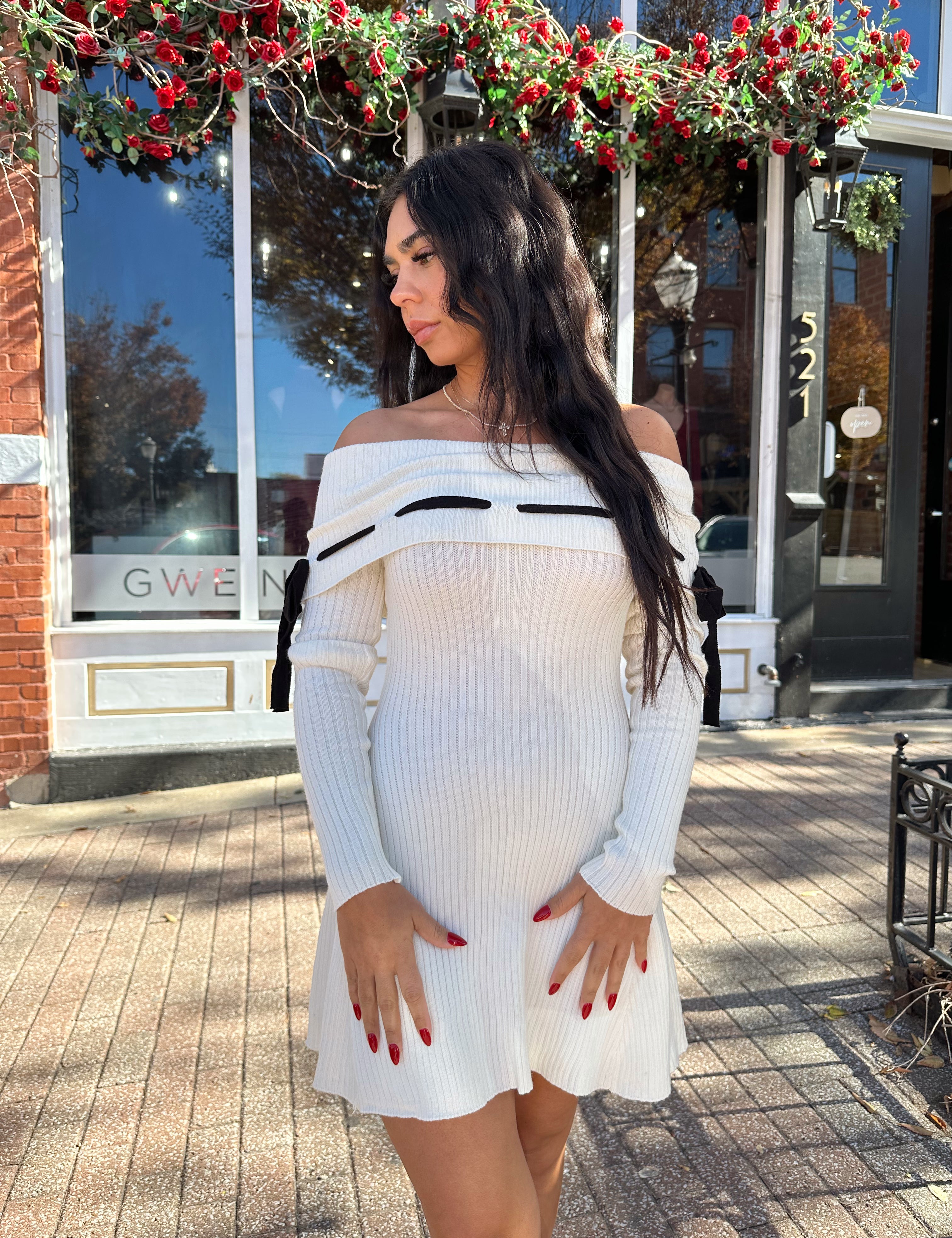 Woman wearing cream off the shoulder sweater mini dress with black tie detail. 