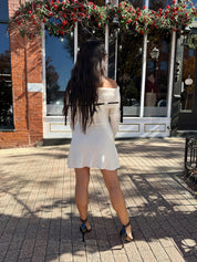 Woman wearing cream off the shoulder sweater mini dress with black tie detail. 