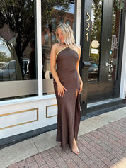 Woman wearing a dark brown satin maxi halter maxi dress with gold trim.