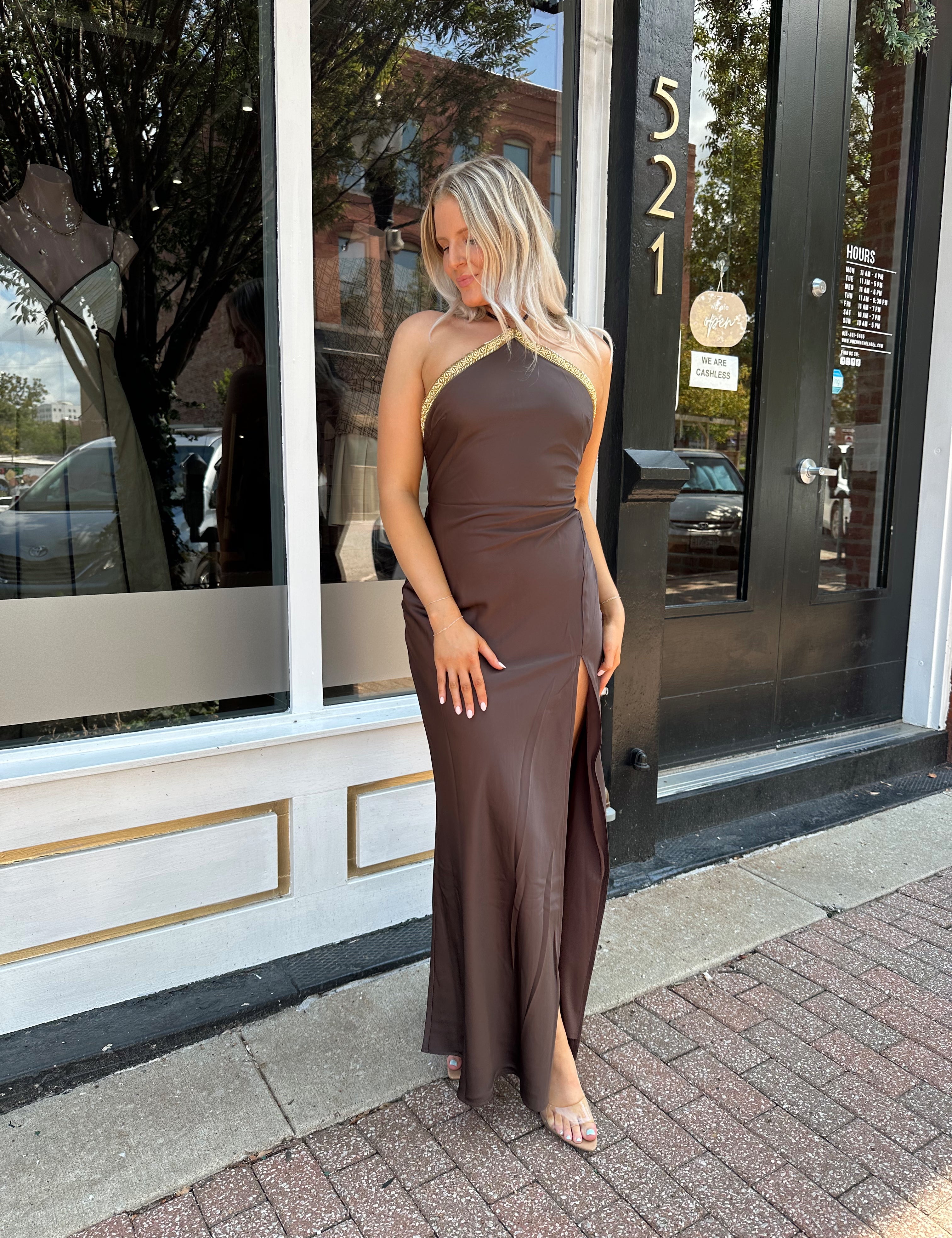 Woman wearing a dark brown satin maxi halter maxi dress with gold trim.